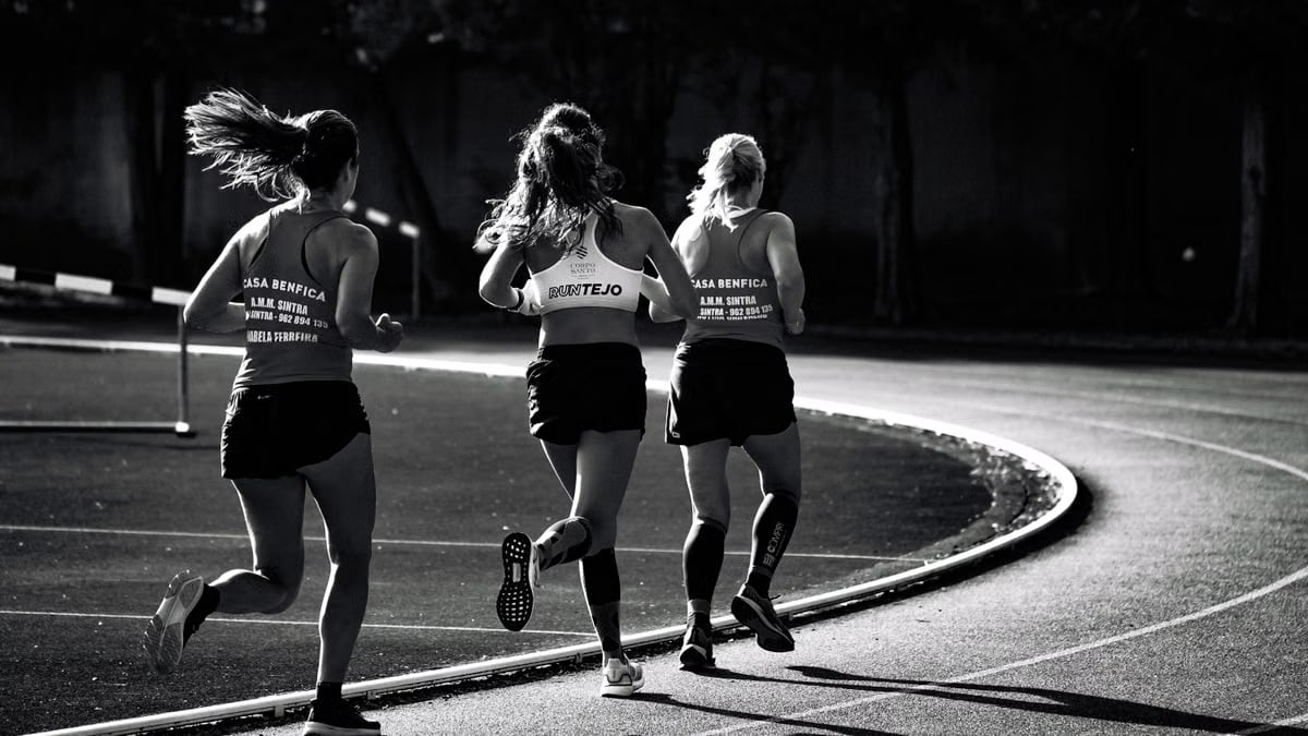 Black and white back view of unrecognizable fit female runners in sportswear running during track and field competition